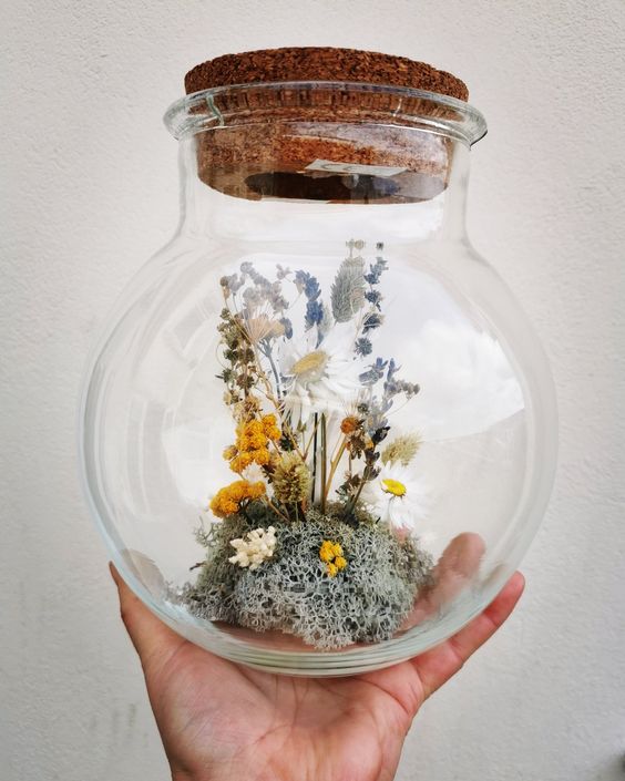 a large jar with a cork lid and some moss, dried neutral, yellow and blue blooms and some berries is a cool idea for quirky home decor