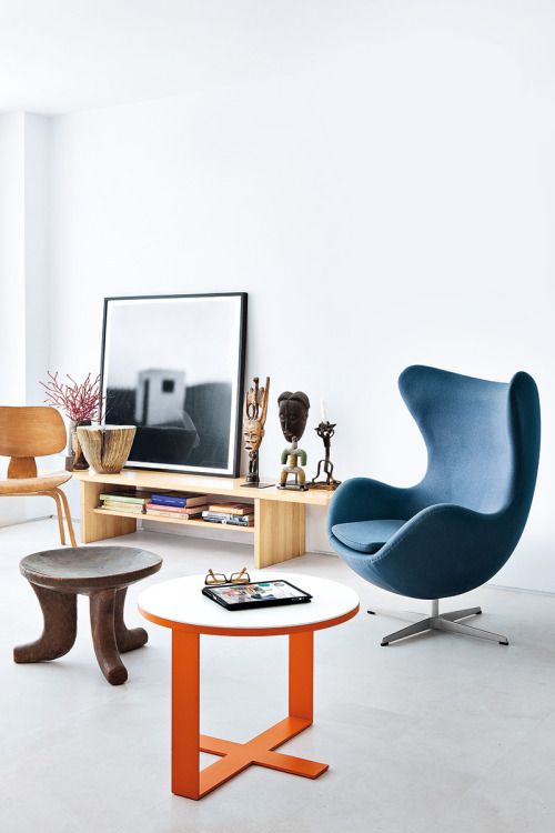 a light-filled and airy space with a blue Egg chair, some mismatching stools, a wooden bench as a console table and some decor