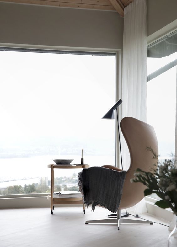 a lovely nook with floor to ceiling windows, a tan Egg chair, a side table, a floor lamp and gorgeous views and air