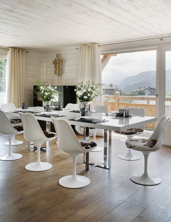 a modern chalet dining room with large windows, a white table, Tulip chairs with printed upholstery, neutral textiles