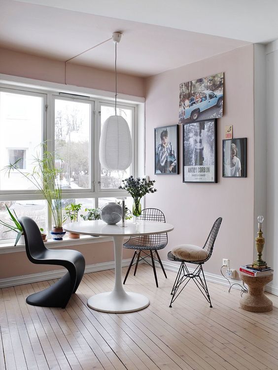 a modern dining space with pink walls, a gallery wall, white table, a sculptural chair and Eames wire chairs, a pendant lamp and some decor