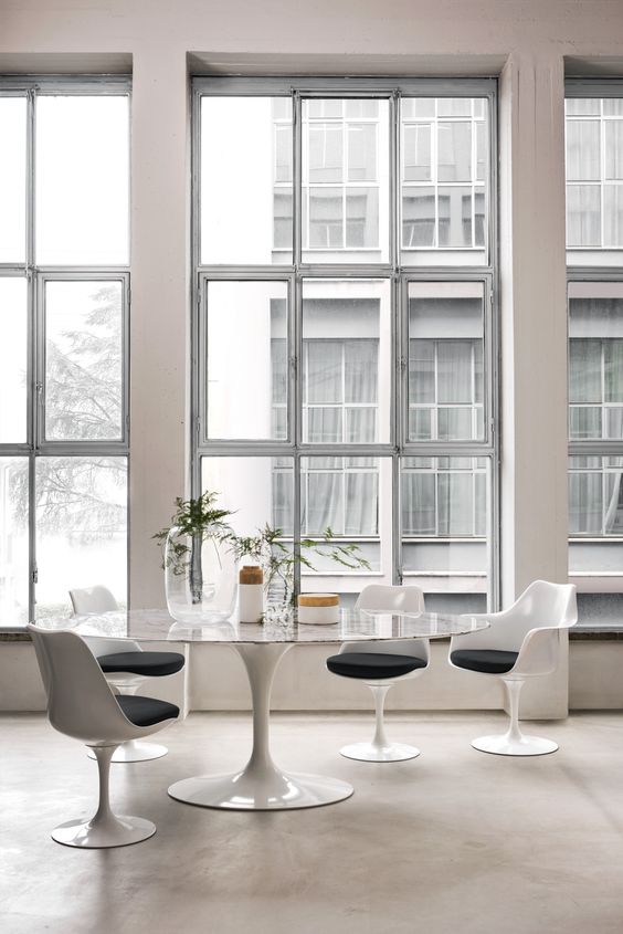 a modern dining space with tall windows, an oval table, graphite grey Tulip chairs and some modern vases