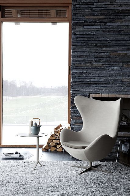 a neutral Egg chair, a white side table, a built-in fireplace, a stack of firewood and a gorgeous view compose a lovely look