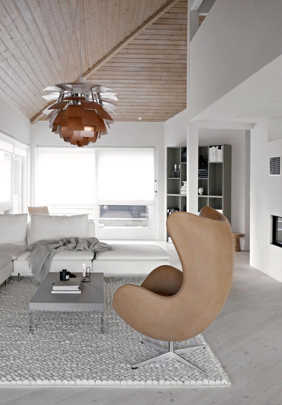 a neutral Scandinavian living room with a creamy corner sofa and a grey coffee table, a brown Egg chair and a pendant lamp