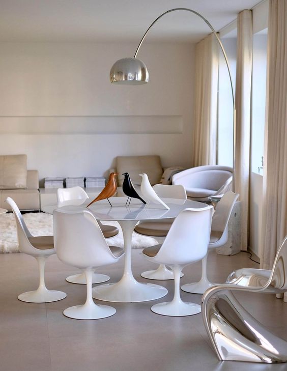 a neutral dining space with a tan sofa and a table, a round table, tan Tulip chairs, a floor lamp and some decor