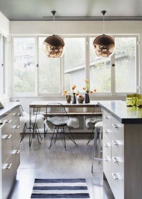 a neutral kitchen with a dining space by the window, with a long table, a bench and Eames wire chairs plus copper pendant lamps