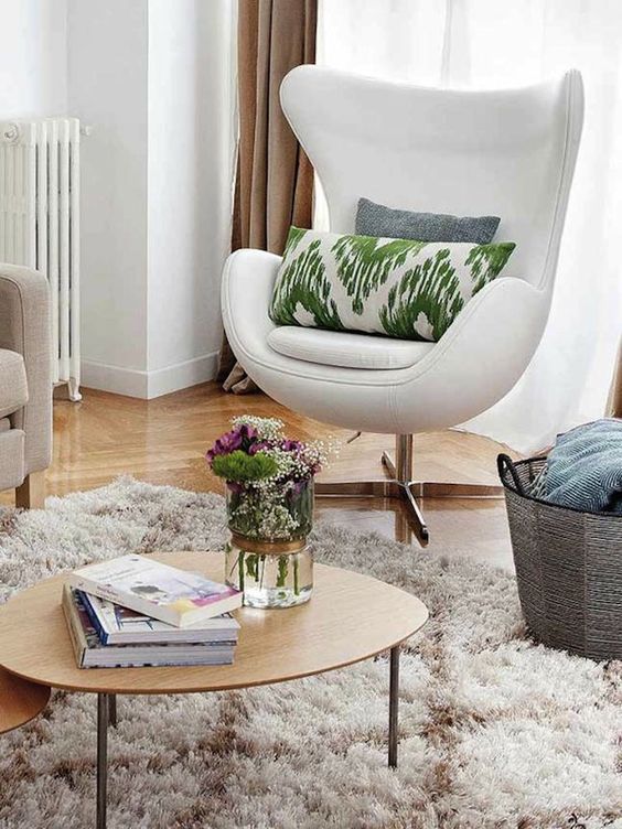 a neutral nook with a sofa, a white Egg chair with printed pillows, a basket, a fluffy rug and a low coffee table