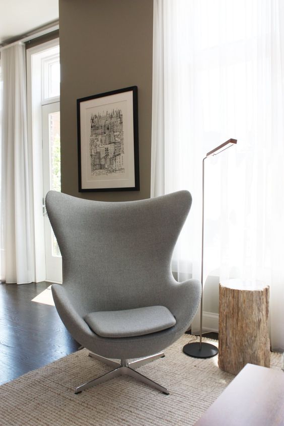 a neutral nook with taupe walls, a grey Egg chair, a stump side table, a floor lamp, a neutral coffee table and a rug