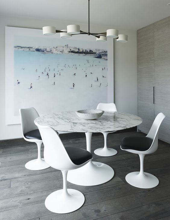 a pretty dining space with an oversized artwork, a round table, black and white Tulip chairs and a cool chandelier