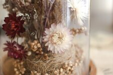 a pretty dried flower terrarium with berries and grass, dried neutral and burgundy blooms and some other grasses on top