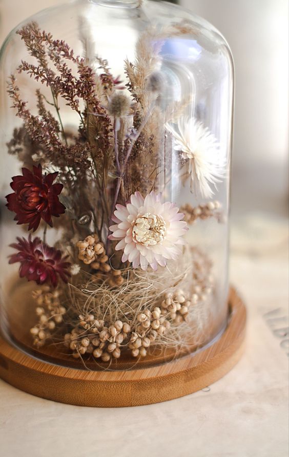 a pretty dried flower terrarium with berries and grass, dried neutral and burgundy blooms and some other grasses on top