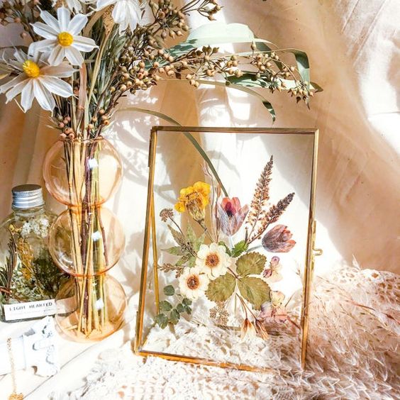 a pretty table art with pressed blooms and leaves in a gold frame is a stylish decoration for summer