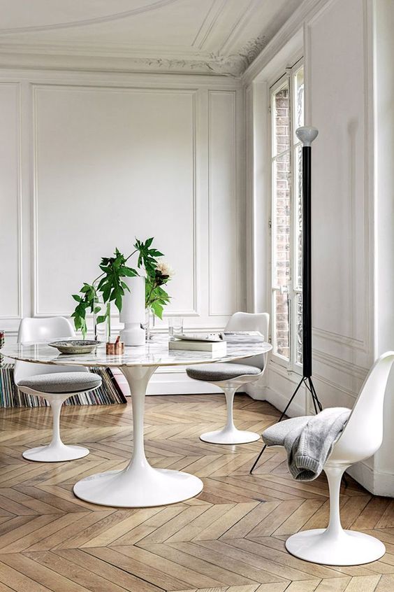 a refined neutral dining space with a Parisian feel, with stucco, a roudn table, grey Tulip chairs and stacks of vinyl