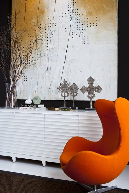 a refined space with an oversized artwork, a white credenza, an orange Egg chair, some vintage decor and branches in a vase