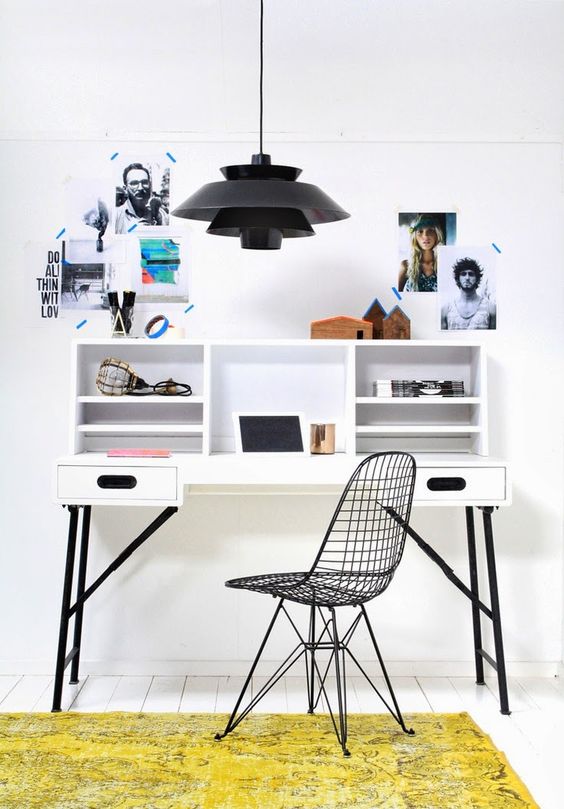 a small and catchy working space with a black and white desk, a black Eames chair, a black pendant lamp and some photos for inspiration