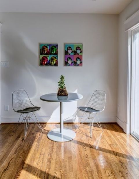a small and cool dining space with a round table, Eames wire chairs, a potted plant and bright artwork is awesome