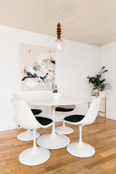a small and stylish dining nook with a round table, black Tulip chairs, a pendant lamp, some potted plants and art