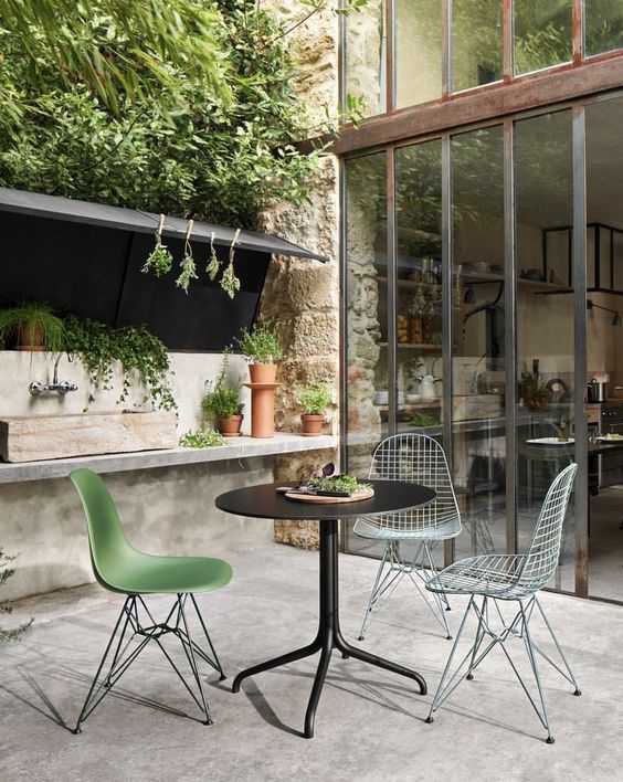 a small outdoor dining space with a black table, Eames chairs including wire ones and a planting station by their side