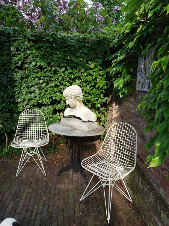a small outdoor space wiht a living wall, a round table with decor and a couple of Eames wire chairs in white