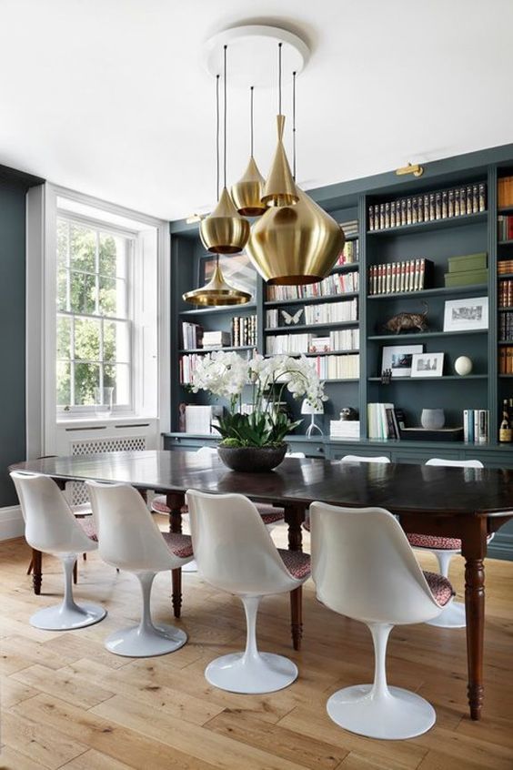a sophisticated dining room with slate grey walls, a large built-in storage unit, a black dining table and Tulip chairs plus a cluster of brass pendant lamps