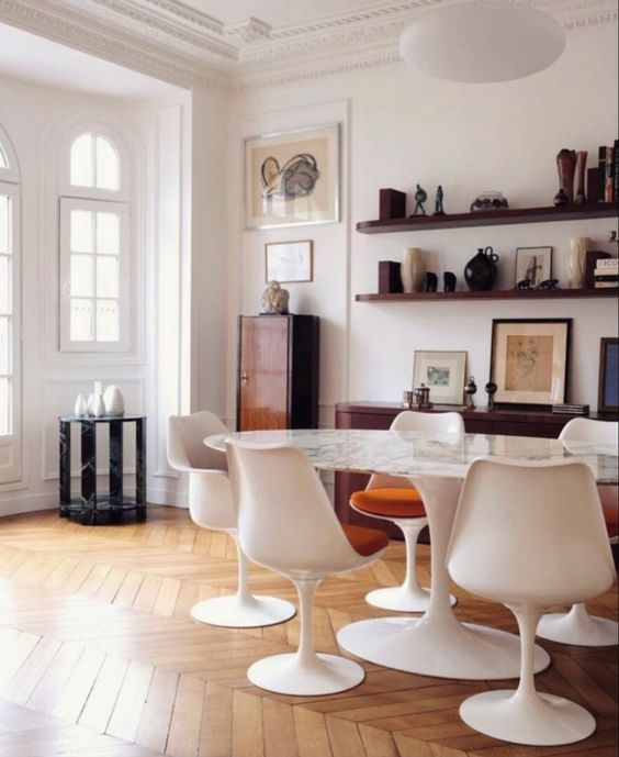 a sophisticated dining space with an oval table, rust-colored chairs, stained shelves, a credenza, a cabinet and some decor and art
