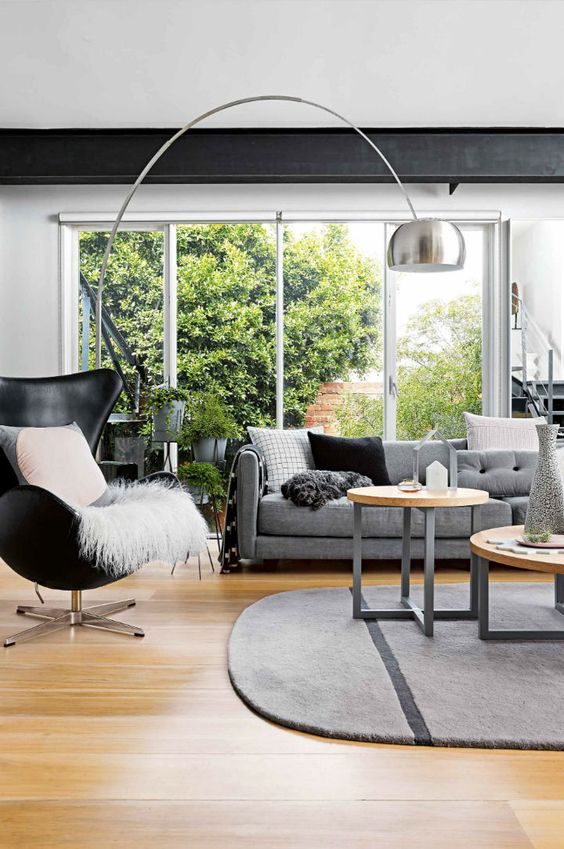 a stylish Scandinavian living room with a black Egg chair and some pillows, a grey sofa, a rug and some coffee tables, a floor lamp