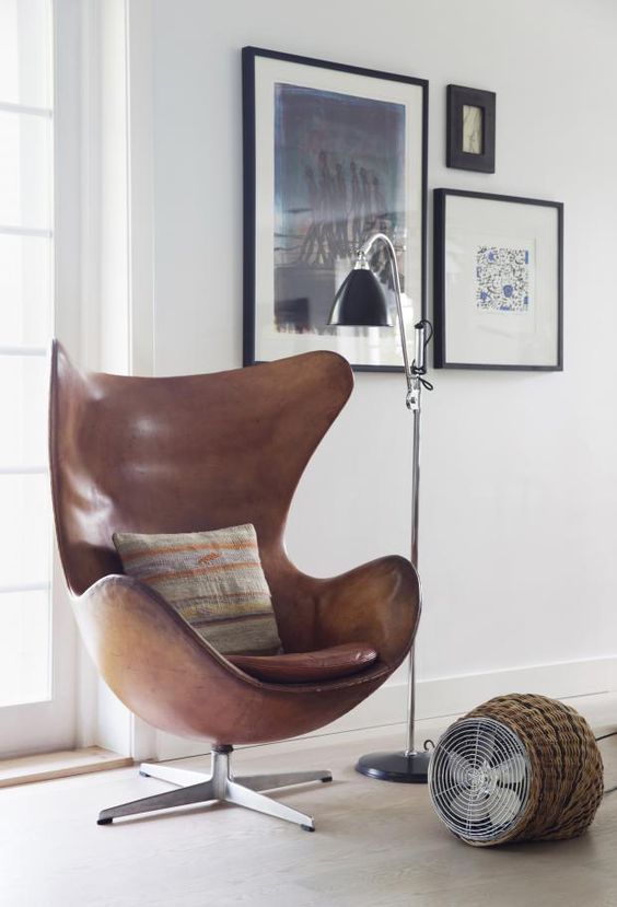 a stylish and catchy nook with a mini gallery wall, a brown leather Egg chair, a floor fan and a black floor lamp