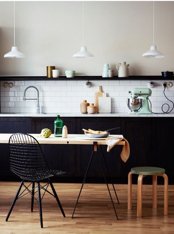 a stylish kitchen with black cabinetry, a white subway tile backsplash, a trestle dining table, an Eames wire chair and some pendant lamps