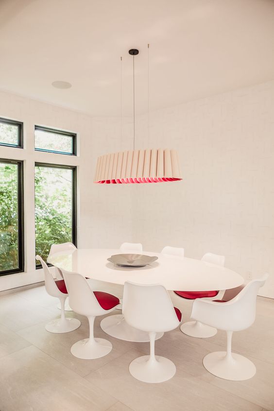 a stylish modern dining space in creamy shades, with a large oval table, pink Tulip chairs, a catchy tube-like chandelier with pink inside