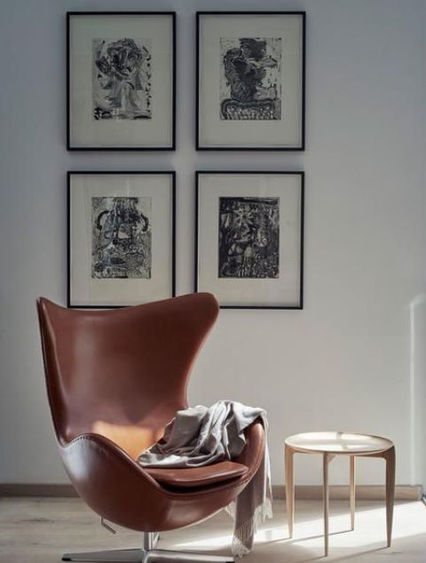 a stylish space with a black and white gallery wall, a brown leather Egg chair, a side table is a cool and elegant space