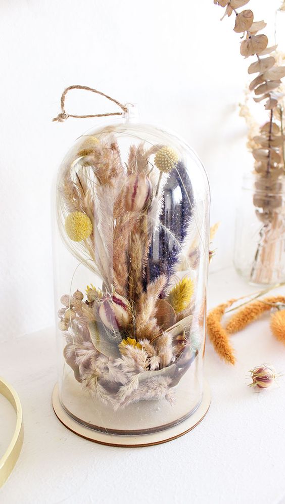a tall cloche with pink and purple dried grasses, billy balls, berries and some lights inside is a pretty and bright decoration