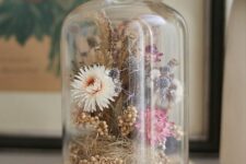 a vintage floral dome with dried moss, berries, blooms in pink and neutrals is a pretty decoration for a boho or vintage space