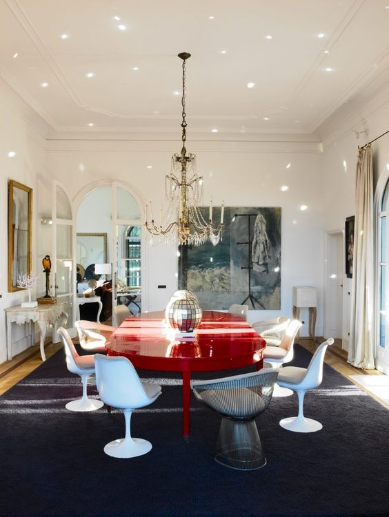 a whimsical dining room with an oversized artwork, a red dining table, neutral Tulip chairs and a metal one, a chic chandelier and a disco ball centerpiece