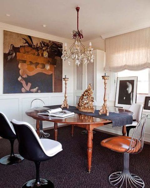 a whimsical dining room with dark artwork, a rich-stained dining table, mismatching chairs including Tulip ones and a chandelier