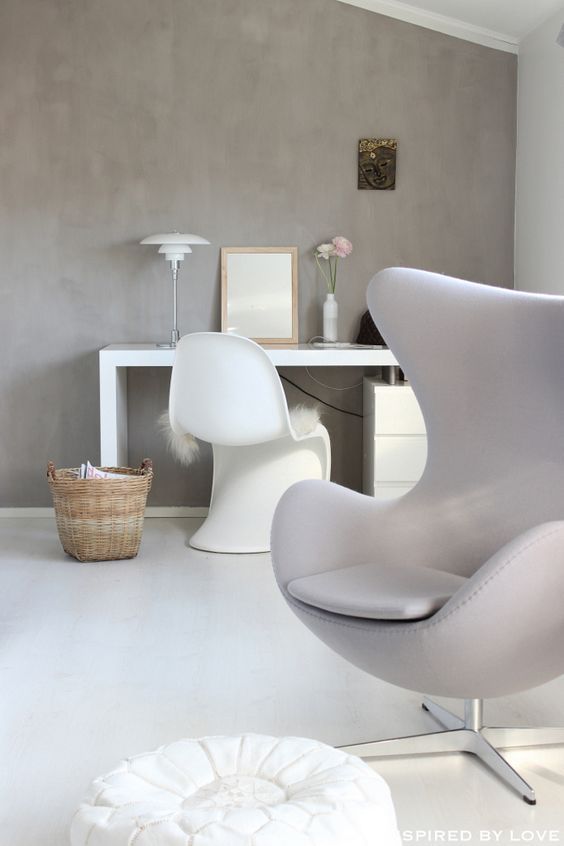 an airy Scandinavian space with a concrete accent wall, a white desk, a white sculptural chair, a grey Egg chair, a lamp and a basket