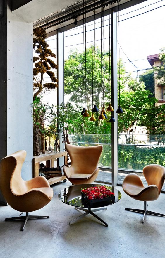 an airy and light-filled space with a glazed wall, a round table, amber leather Egg chairs and a cluster of tiny pendant lamps