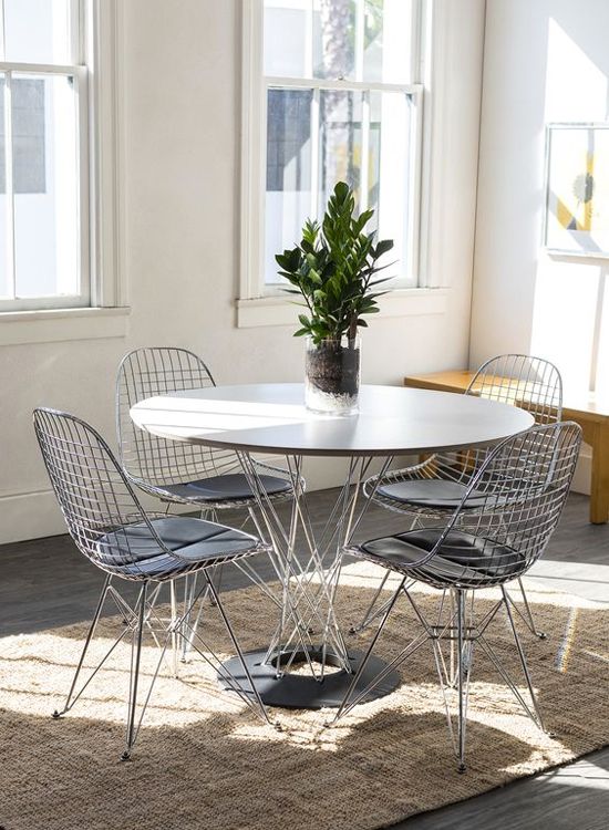 an airy dining space with a yellow bench, a round table, Eames wire chairs and a potted plant plus a rug and an artwork