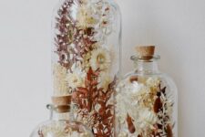 an arrangement of three glass bottles with a matching design, with dried blooms and leaves is a beautiful boho home decor idea