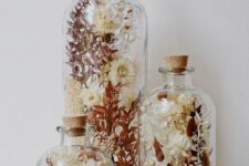 an arrangement of three glass bottles with a matching design, with dried blooms and leaves is a beautiful boho home decor idea
