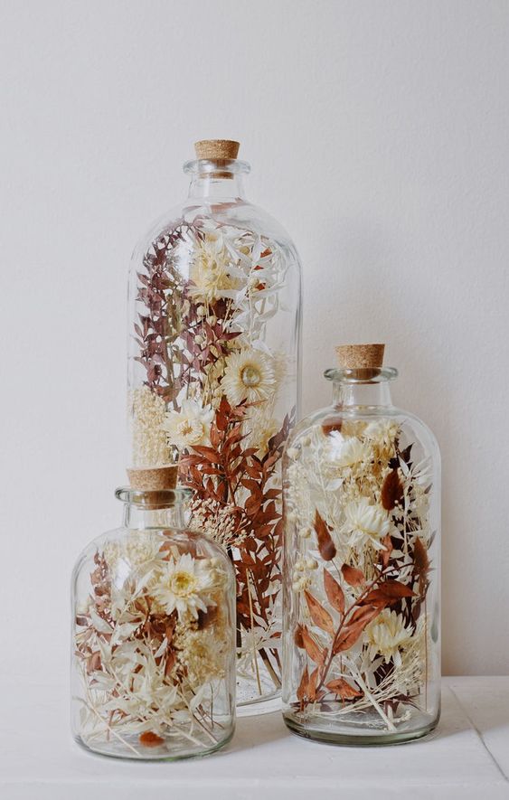 an arrangement of three glass bottles with a matching design, with dried blooms and leaves is a beautiful boho home decor idea