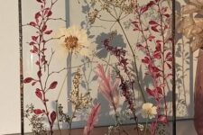 an arrangement of white and pink blooms and leaves in a frame on a stand is a lovely decoration that can be hung or placed on the table