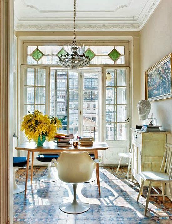 an eclectic dining room with neutral walls and stucco, a stained table, navy Tulip chairs, a chic chandelier and some vintage decor