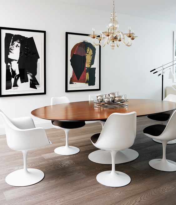 an elegant dining room with an oval table and black and white Tulip chairs, a mini gallery wall and a gilded chandelier