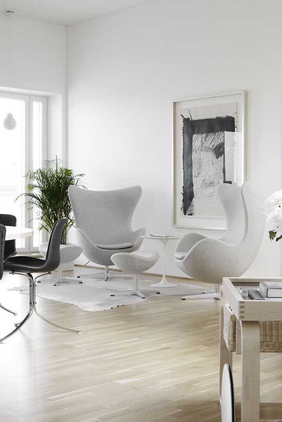 an ethereal space with an oversized artwork, light grey Egg chairs, a neutral rug, a potted plant and a coffee table