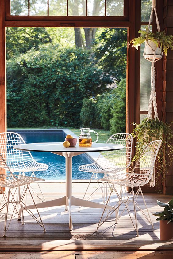 an indoor-outdoor dining space with a round table, white Eames wire chairs and some potted plants hanging down