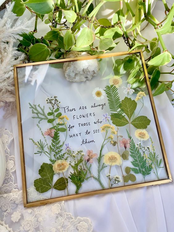 pressed yellow and pink blooms and leaves in a gold frame, with some words, are a cool botanical decoration for any space
