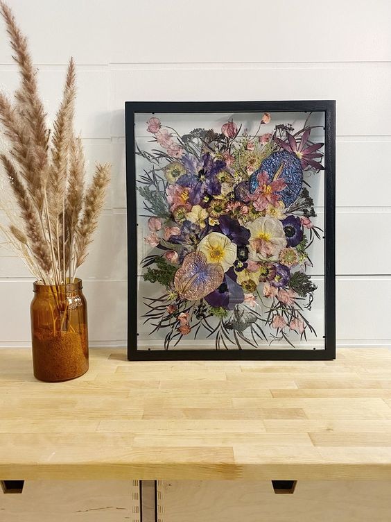 purple, pink and yellow pressed flowers plus leaves in a black frame are a cool decoration for any space with color