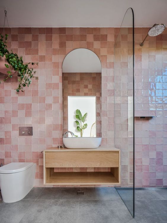 02-a-beautiful-bathroom-clad-with-pink-zellige-tiles-a-shower-a-floating-vanity-an-arched-mirror-and-some-greenery.jpg