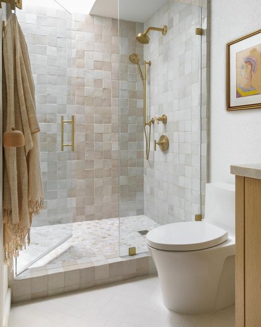 04-a-catchy-and-light-filled-neutral-bathroom-clad-with-neutral-Zellige-tiles-a-skylight-over-the-shower-white-appliances-and-gold-fixtures.jpg