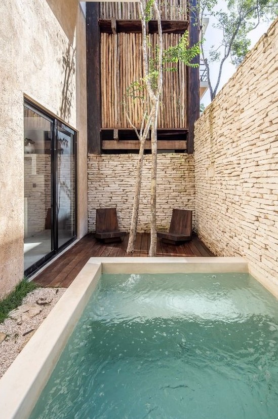 08-a-minimal-outdoor-space-with-stone-walls-a-dark-stained-furniture-a-plunge-pool-some-trees-and-wooden-chairs.jpg